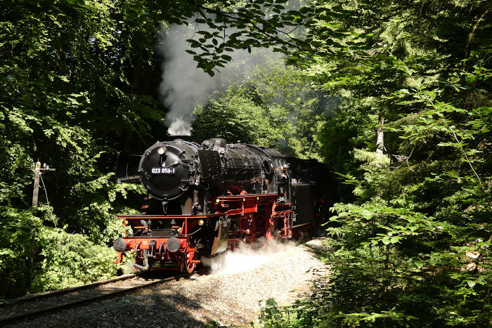 23&nbsp;058 + 64&nbsp;419 vor dem regulären Zug von Schorndorf nach Welzheim hinter Laufenmühle im Wald (bei Km&nbsp;17,7), um 11:28h am 27.06.2021