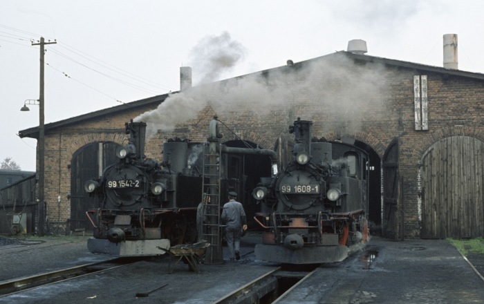 99&nbsp;1542 neben 99&nbsp;1608 in einer Ruhepause und beim Restaurieren an vielfotografierter Stelle vor den Schuppentoren in Mügeln, am Nachmittag des 26.10.1977