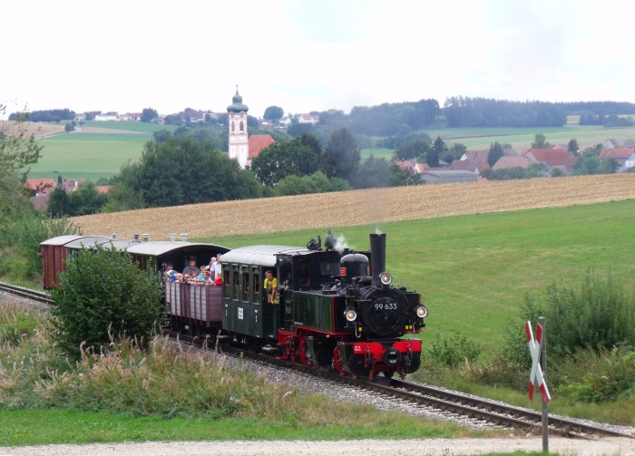 99&nbsp;633 mit Zug Ochsenhausen-Warthausen, am Feldweg-Bahnübergang am Waldrand oberhalb von Reinstetten mit Kirche Reinstetten im Hintergrund, um 13:43h am 13.09.2015