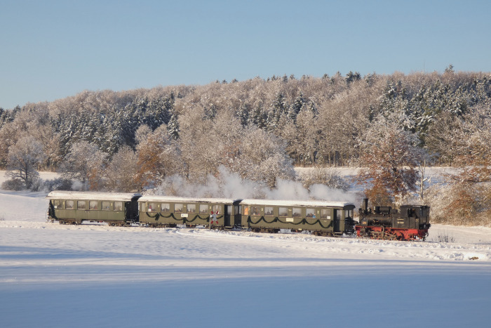99&nbsp;7203&nbsp;Tv mit Nikolauszug auf Talfahrt zurück von Oppingen nach Amstetten an einem schneebedeckten Feldweg-Bahnübergang am oberen Duital, um 15:14h am 03.12.2023
