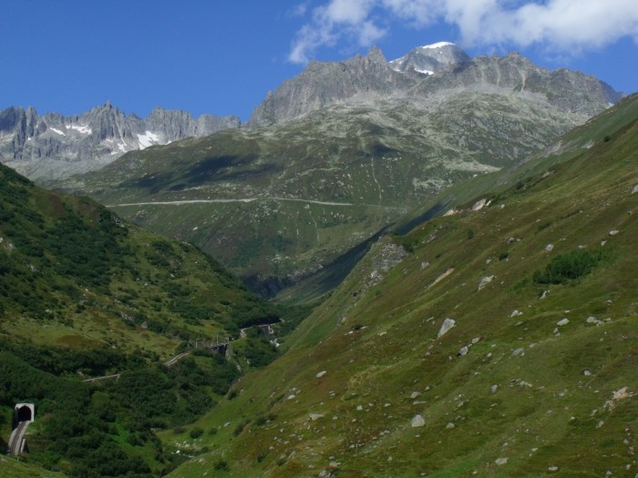 Links am Talrand der Alt Senntumstafeltunnel&nbsp;I (der oberste von den drei Tunneln), dahinter die Klappbrücke vom Steffenbachtal und ganz hinten am Berghang die Stützmauer der Paßstraße vor der Kulisse der Berggipfel am Furkapass