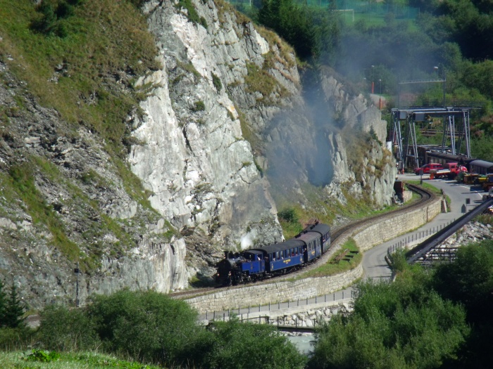 DFB&nbsp;1 mit erstem Zug Realp-Oberwald des Tages, hinter dem Betriebswerk der DFB, an der Felswand und der laut rauschenden Reuss 10:20h am 30.08.2015