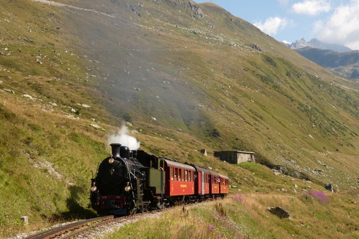 Lok 704 DFB mit dem ersten Zug des Tages (Nr.133) Realp-Oberwald, fotografiert etwa bei Streckenkilometer&nbsp;52,7 unterhalb vom Bahnhof Furka, um 10:51h am 11.08.2022