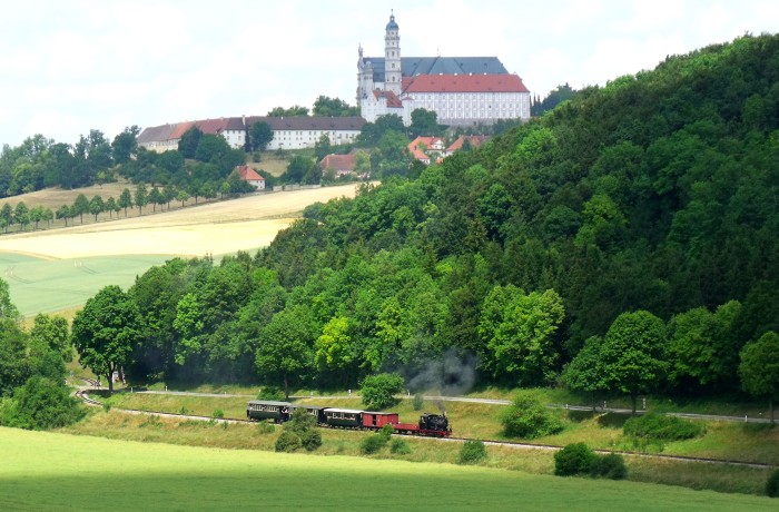 WN&nbsp;12 mit Zug P&nbsp;3 Neresheim&rarr;Sägmühle am Egautal, mit dem berühmten Kloster im Hintergrund, um 13:18h am 19.06.2014