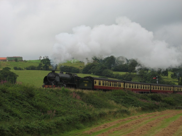 825 mit Zug aus Whitby nach Pickering nimmt Anlauf in die Steigung hinter den “sheds” hinter Grosmont, fotografiert von der Wiese gegenüber den Esk&nbsp;Valley Cottages, um 14:39h am 18.08.2008